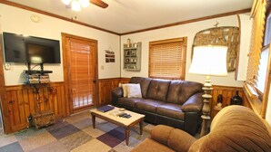 A living room with a brown leather sofa, a coffee table, a television, and a lamp. - Creekside Treehouse- Creekside Cabin (Bryson City)