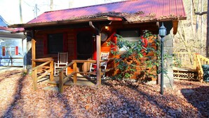 A cabin with a red roof, wooden porch, and a small garden area. - Creekside Treehouse- Creekside Cabin (Bryson City)