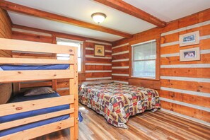 Ein Blockhauszimmer mit einem Etagenbett, einem Einzelbett mit einem gemusterten Quilt, Holzwänden und zwei gerahmten Bildern.