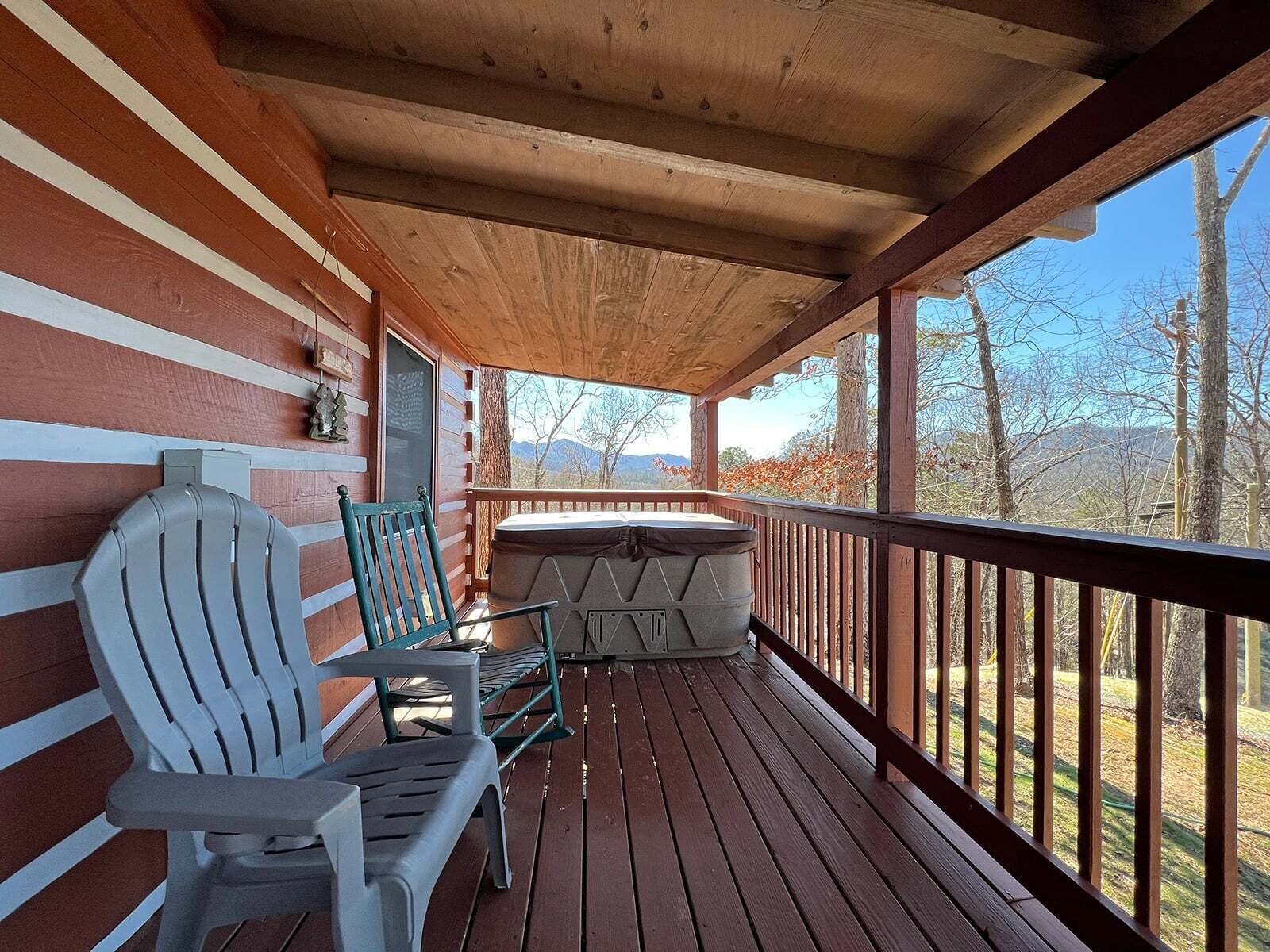 Eine Holzterrasse mit Whirlpool, zwei Adirondack-Stühlen und Blick auf Bäume und Berge.