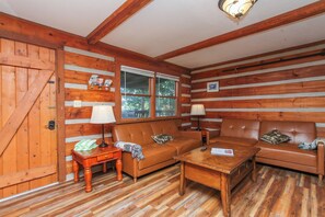 Ein Holzblockhaus-Interieur mit Holzboden, einer Couch, einem Tisch und einem Fenster.