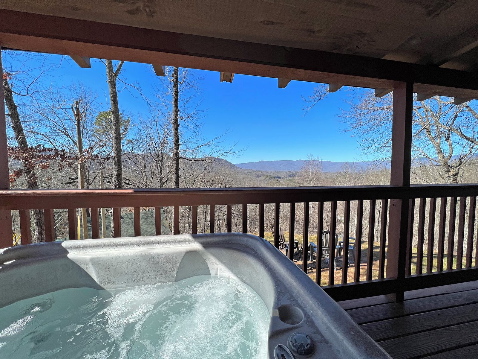 Un bain à remous sur une terrasse en bois, avec vue sur les montagnes et les arbres.