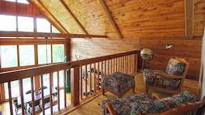 Interior de uma cabana de madeira com varanda, piso de madeira e área de jantar.