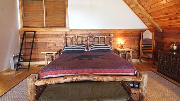 Quarto estilo loft com estrutura de cama de madeira, escada, mesinha e cômoda.