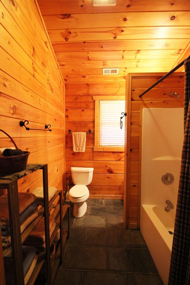 A wooden cabin bathroom with a toilet, a bathtub, and a window.