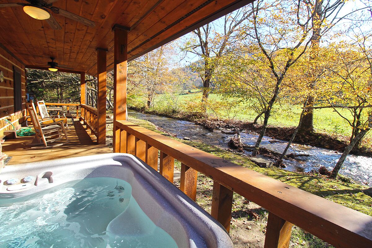 A wooden deck with a hot tub, overlooking a stream and autumn foliage.