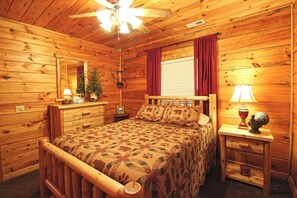 Ein Schlafzimmer einer Holzhütte mit Bett, Nachttischen, Deckenventilator und einem Fenster mit Vorhängen.