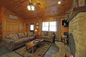 Ein Holzblockhaus-Innenraum mit Kamin, zwei Sofas, einem Couchtisch und einem Deckenventilator.
