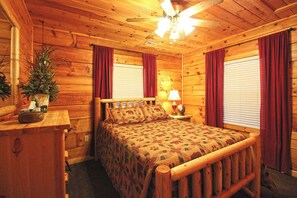 Ein Schlafzimmer in einer Holzhütte mit einem Bett, einem Nachttisch, einer Lampe und einem Deckenventilator.