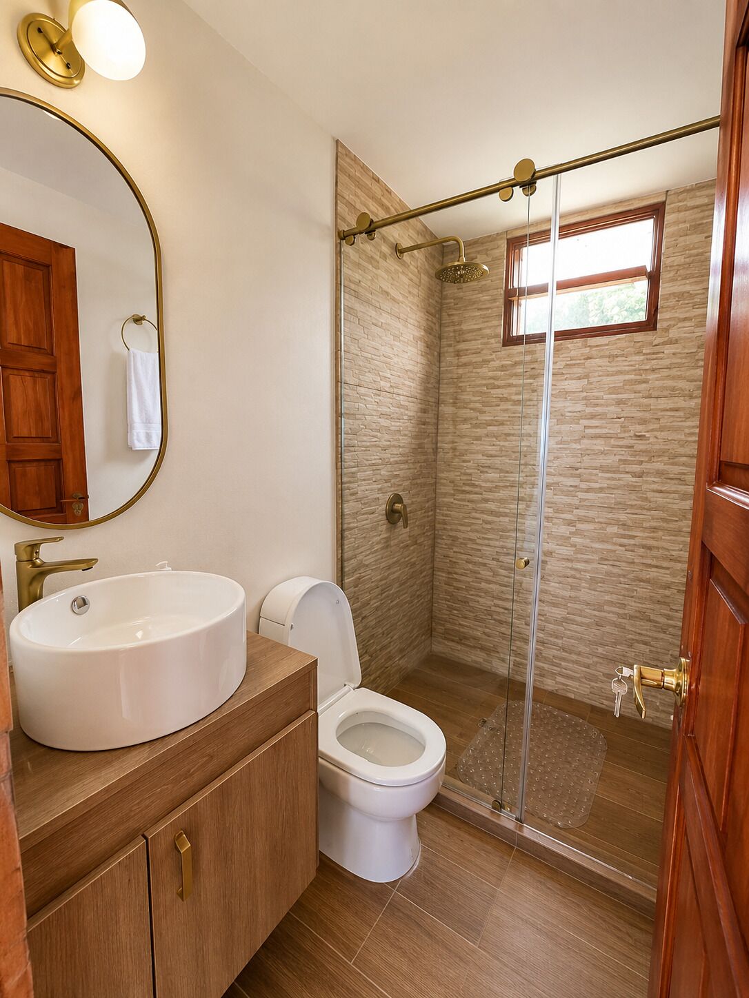 A bathroom with a large oval sink, a toilet, a glass-enclosed shower, and a wooden vanity.