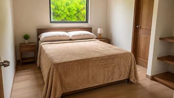 Ein Schlafzimmer mit einem Bett, einem Nachttisch, einem Fenster mit Blick auf Grünflächen und einer Holzbalkendecke.