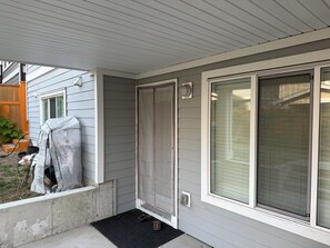 En entré till ett bostadshus med en skjutdörr av glas, ett trappsteg av betong och en svart dörrmatta.