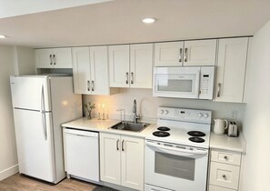 A compact kitchen with white cabinetry, a built-in microwave, a stove, and a refrigerator. - A bright, clean walking-out basement unit in Surrey,near White-rock. (Surrey)