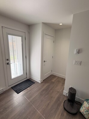 A clean, modern hallway with a wooden floor, a door with a glass panel, and a small area rug. - A bright, clean walking-out basement unit in Surrey,near White-rock. (Surrey)