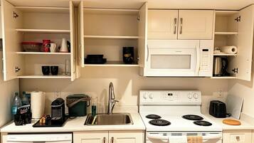 A compact kitchenette with a microwave, stove, sink, and a dish drying rack.