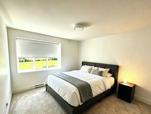 A bedroom with a bed, a nightstand, a window with a view of a green field, and a ceiling light. - A bright, clean walking-out basement unit in Surrey,near White-rock. (Surrey)