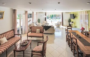 Ein großzügiger Wohnbereich mit einer Couch, Sesseln, einem Esstisch und Blick ins Freie.