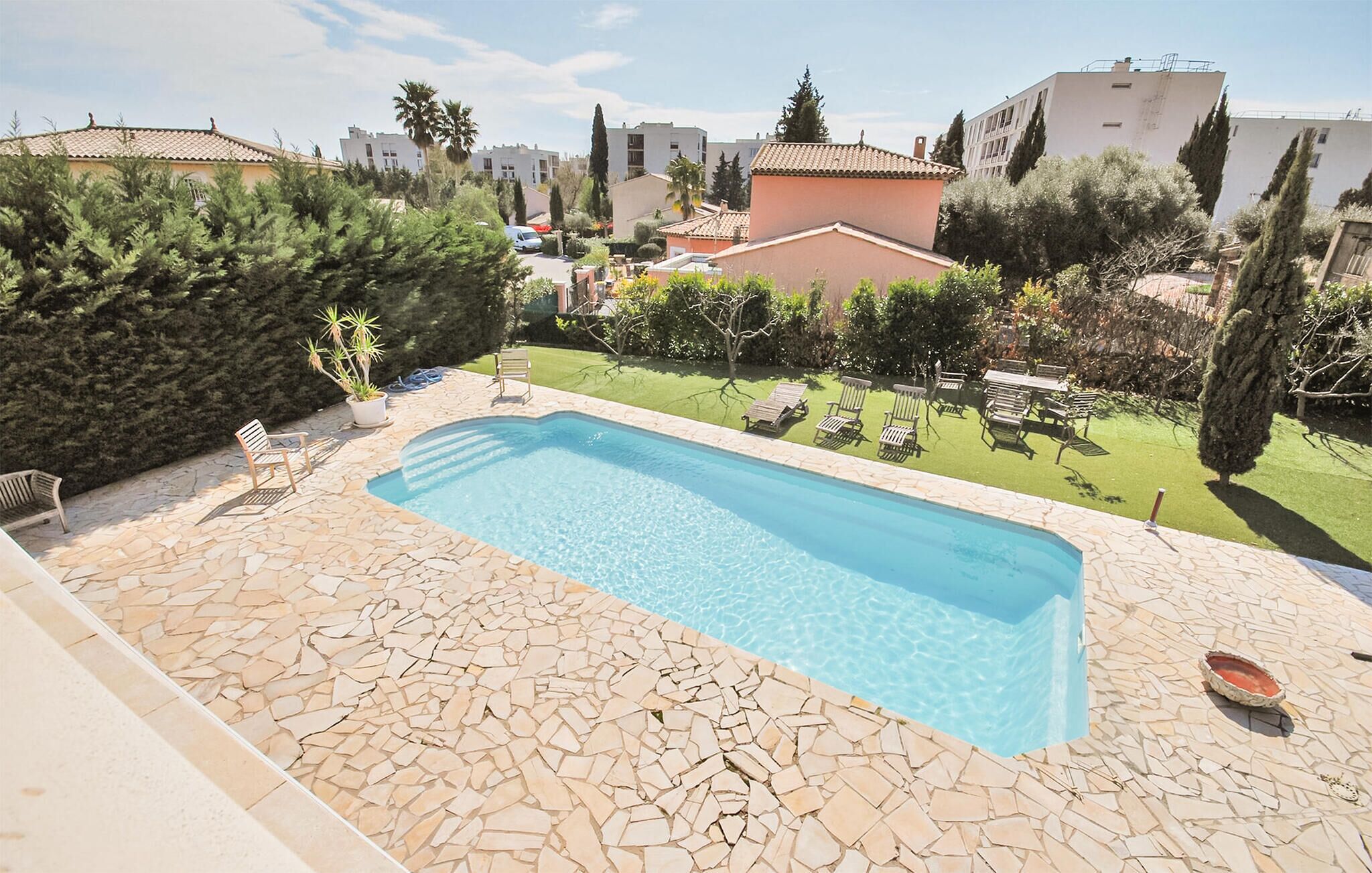 A rectangular swimming pool with a stone mosaic border, surrounded by a lawn and various trees.