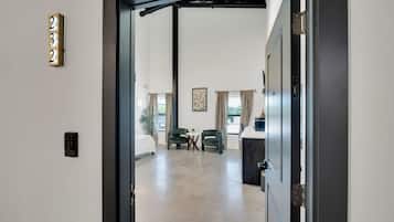 A hotel room with a bed, two chairs, a small table, a desk, a painting on the wall, and a door with a number sign.