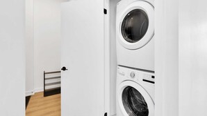 A laundry room with two stacked washing machines, a metal drying rack, and a wooden floor. - Brampton Modern Condo by GO Station (Brampton)