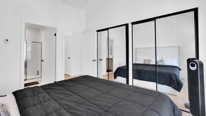 A modern bedroom with a large bed, a walk-in closet, and a sliding door mirror. - Brampton Modern Condo by GO Station (Brampton)