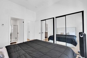Ein modernes Schlafzimmer mit einem großen Bett, einem begehbaren Kleiderschrank und einem Spiegel mit Schiebetür.