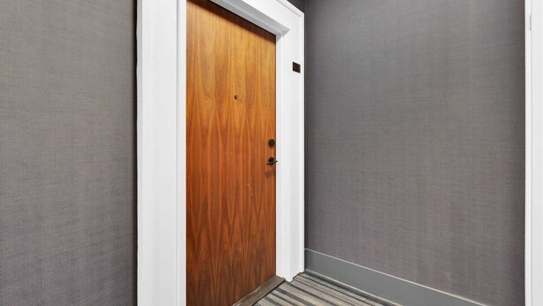 A hallway with a wooden door, grey walls, and a striped carpet. - Brampton Modern Condo by GO Station (Brampton)