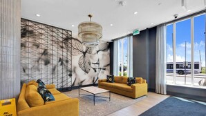 A modern lobby with two sofas, a coffee table, a large wall mural, and a view of the outside. - Brampton Modern Condo by GO Station (Brampton)