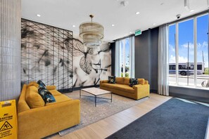 Eine moderne Lobby mit zwei Sofas, einem Couchtisch, einem großen Wandbild und Blick ins Freie.