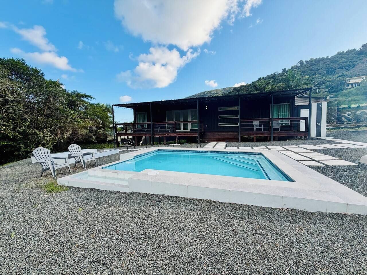 Ein modernes Haus mit Swimmingpool, Sitzgelegenheit im Freien und Blick auf eine hügelige Landschaft.