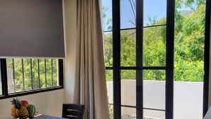 A room with a table, chairs, a fruit basket, and a large window with a view of greenery. - Eco House | Private and Quiet Loft | Perfect for Long Stays (Taganga)
