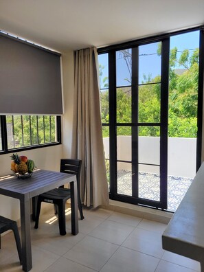 Ein Zimmer mit Tisch, Stühlen, einer Obstschale und einem großen Fenster mit Blick auf Grünflächen.