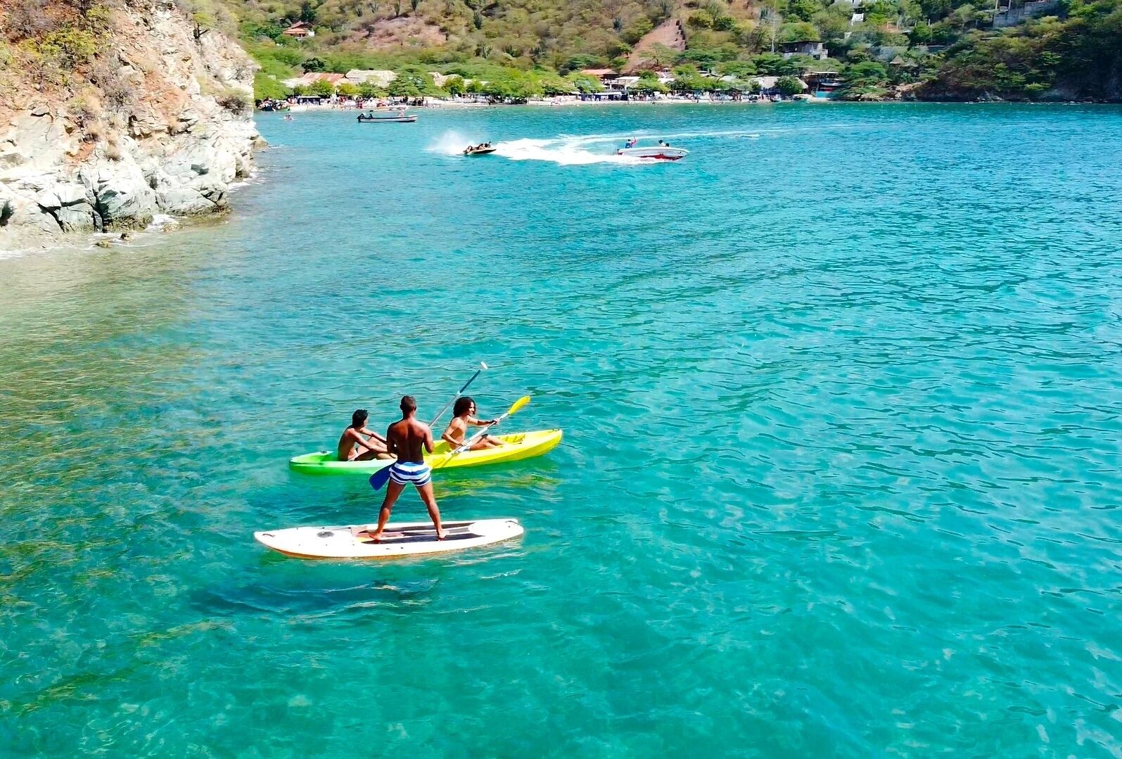 A clear turquoise sea with people paddleboarding and kayaking.