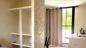 A bedroom with a bed, a white wardrobe, a stone accent wall, a window with curtains, and a kitchenette area. - Eco House | Private and Quiet Loft | Perfect for Long Stays (Taganga)