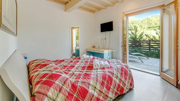 Ein Schlafzimmer mit Bett, Fernseher, Badezimmer und einer Glastür zu einem Balkon.