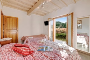 Un dormitorio con cama, armario de madera, televisor y puerta corrediza de vidrio que da a un jardín.