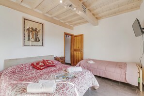 A bedroom with a large bed, a smaller bed, a wooden door, a wall-mounted TV, and a ceiling with wooden beams. - Family Home Margherita Pool Mugello 4, Vicchio, Italy (Vicchio)