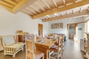 Un comedor con una mesa de madera dispuesta para cuatro personas, rodeada de sillas de madera. Se ve un sofá y un mueble pequeño al fondo.
