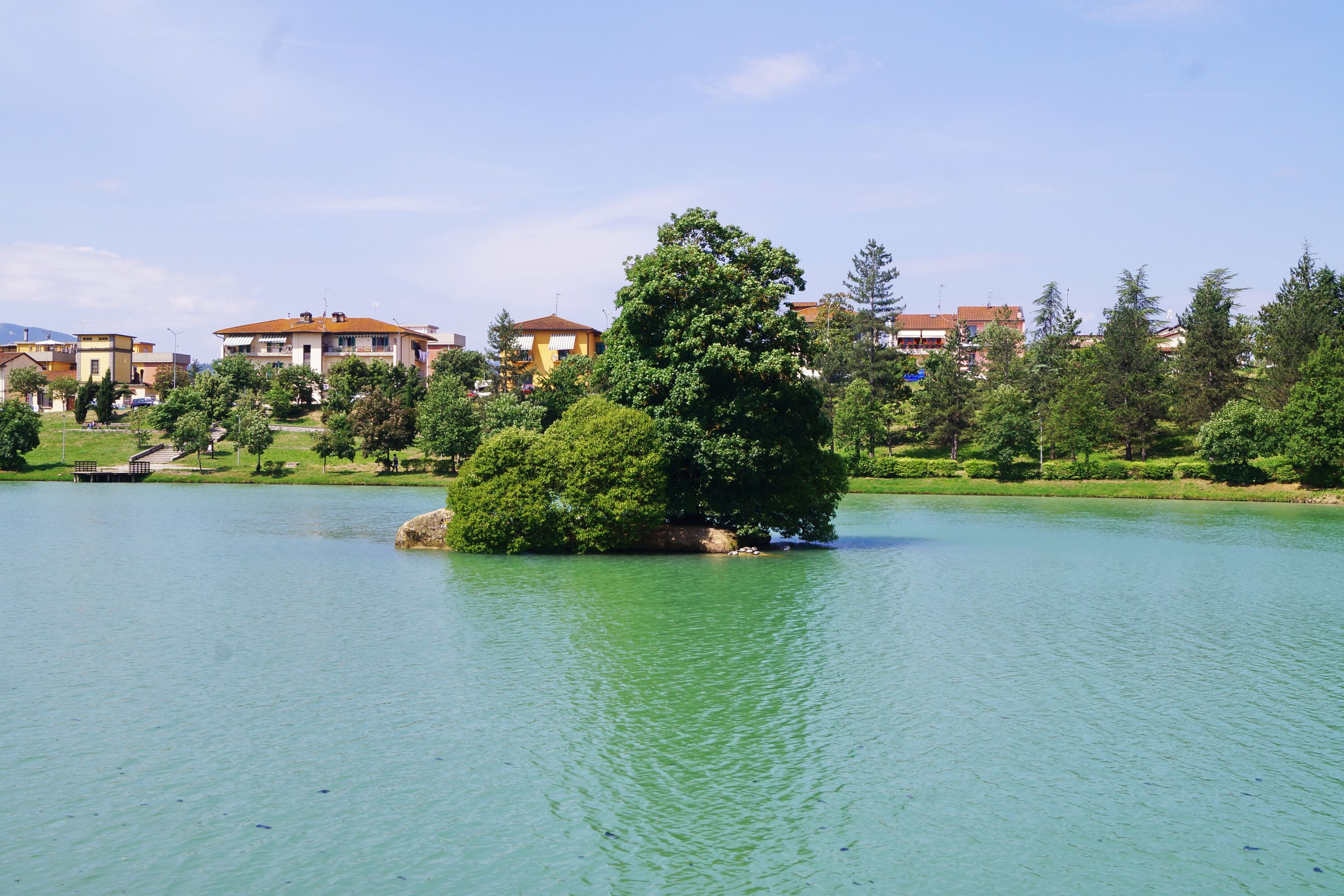 Un lago con una pequeña isla, rodeado de edificios residenciales y vegetación.
