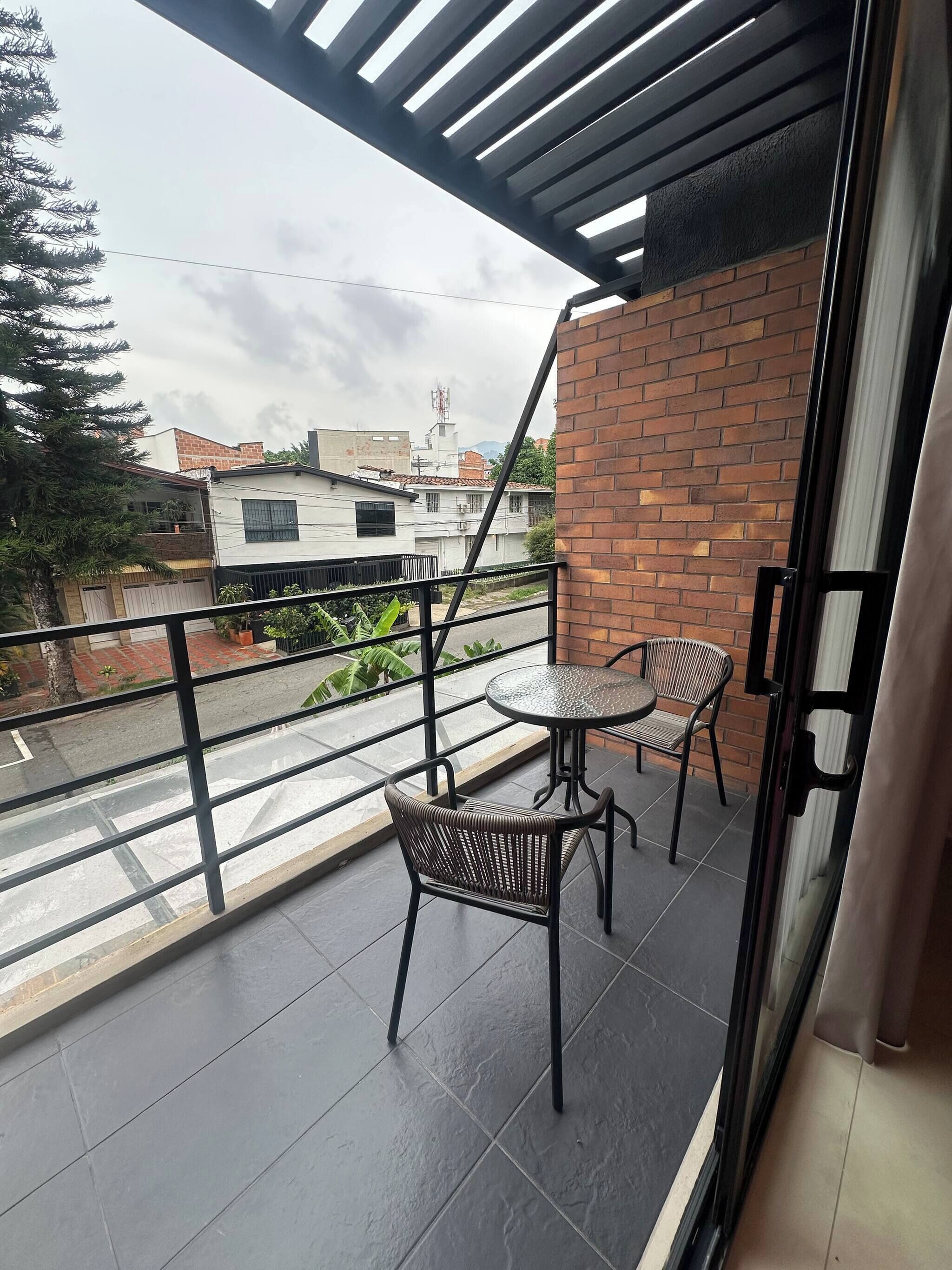 A balcony with two chairs and a table, a brick wall, and a view of buildings and trees.
