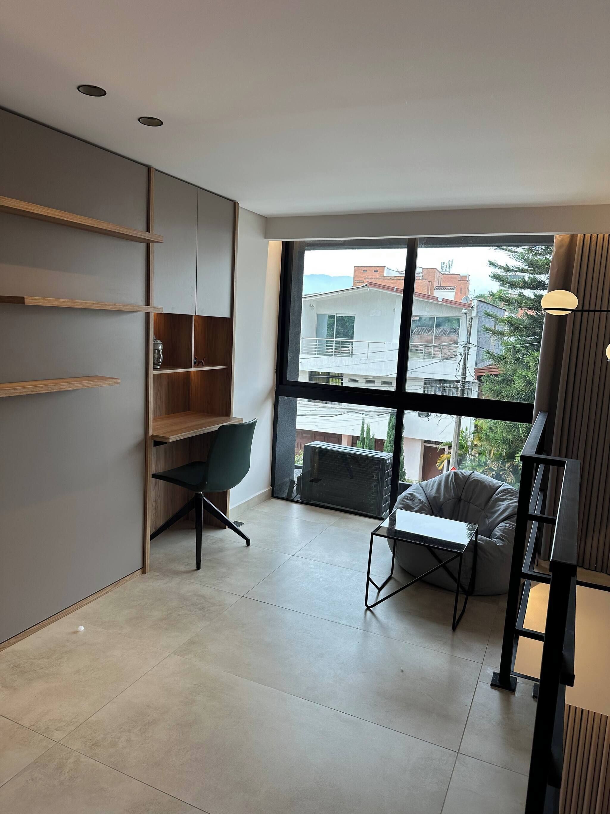Una habitación moderna con un ventanal grande, un escritorio, una silla y estanterías integradas.