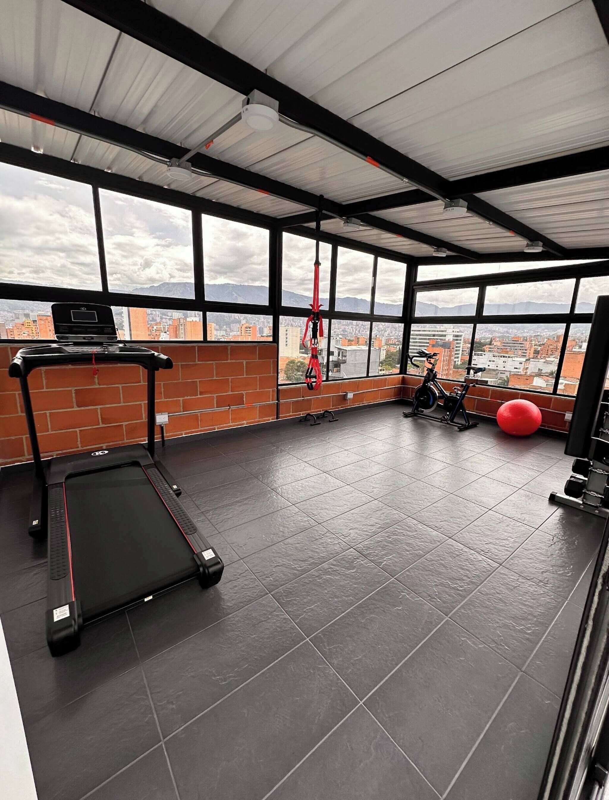 A gym with a treadmill, exercise balls, and a view of a cityscape through large windows.