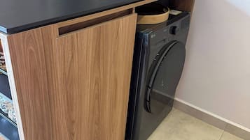 Une cuisine compacte dotée d’un lave-linge encastré, de meubles en bois et d’un plan de travail noir.