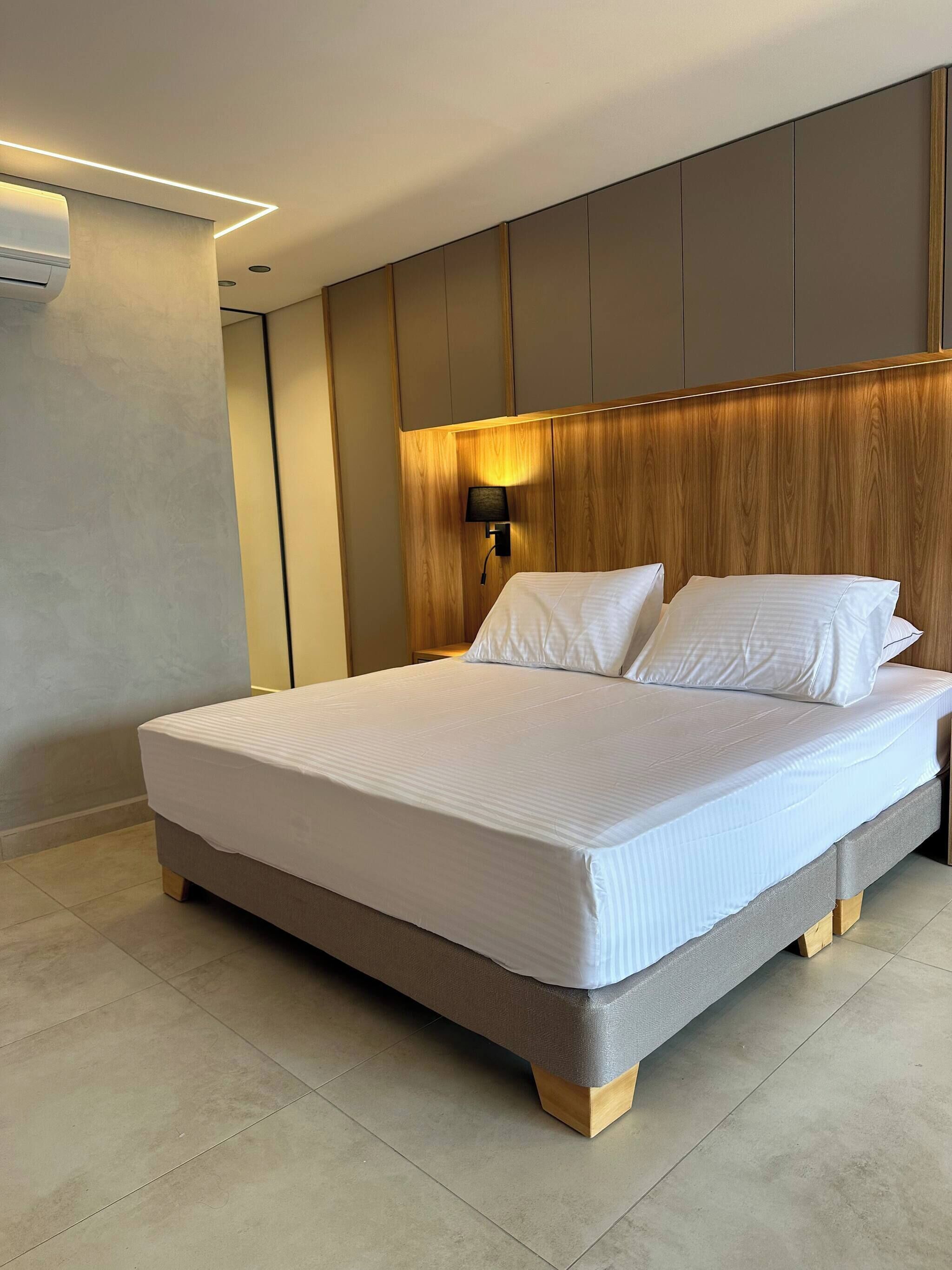 Una habitación de hotel moderna con una cama grande, cabecero de madera y una lámpara fijada a la pared.