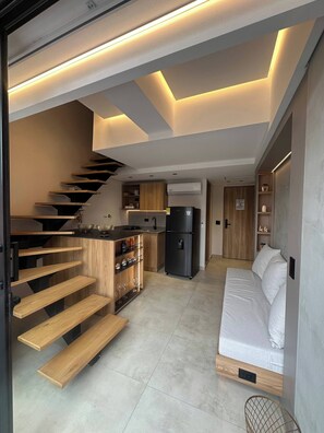 A modern kitchen with a built-in stove, a refrigerator, and a wooden staircase leading to a loft area. - Luxury Duplex Loft AC Rooftop Jacuzzi Laureles (Medellín)