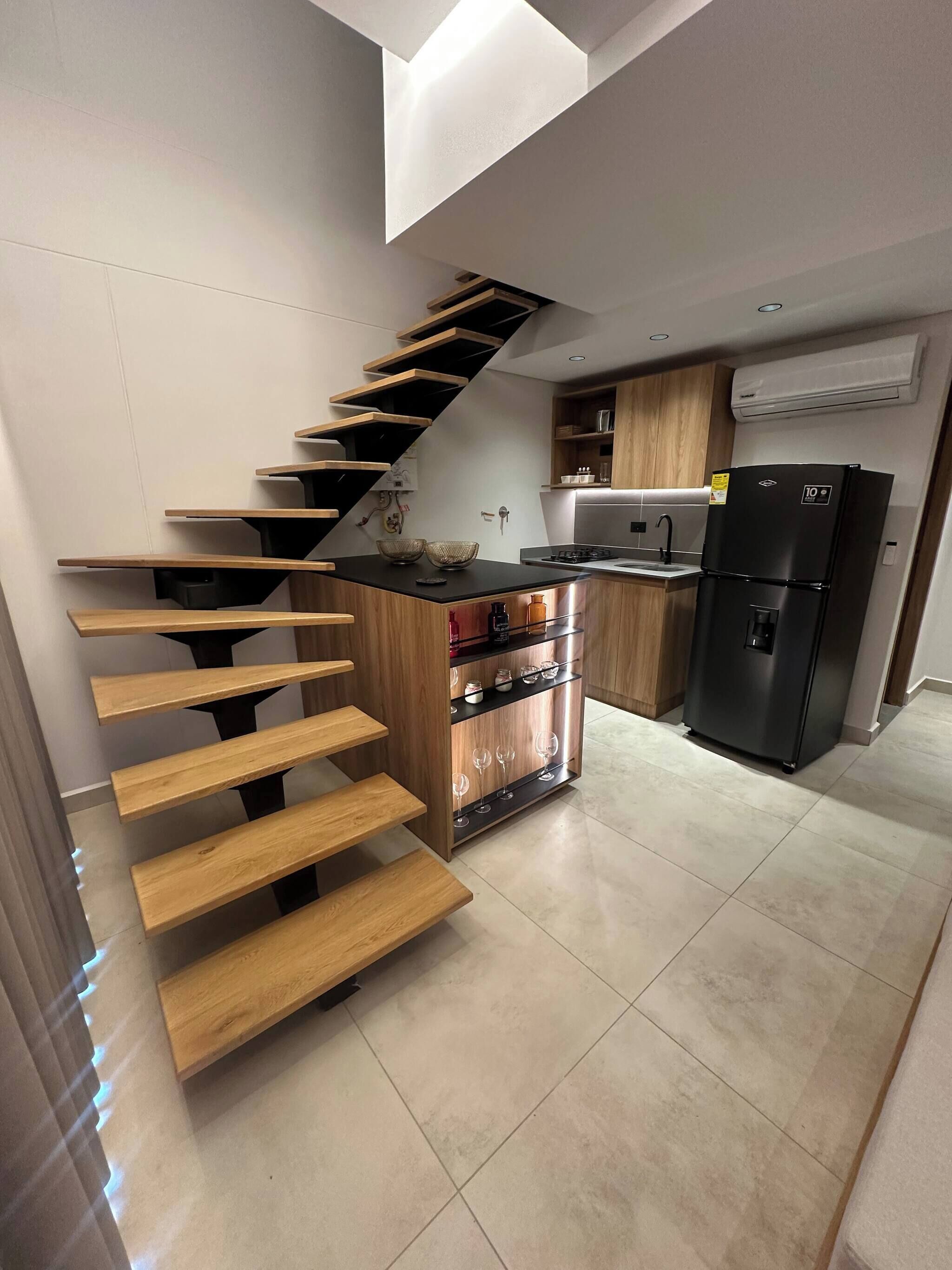 A modern kitchen with a wooden staircase, a black refrigerator, and a built-in wine rack.