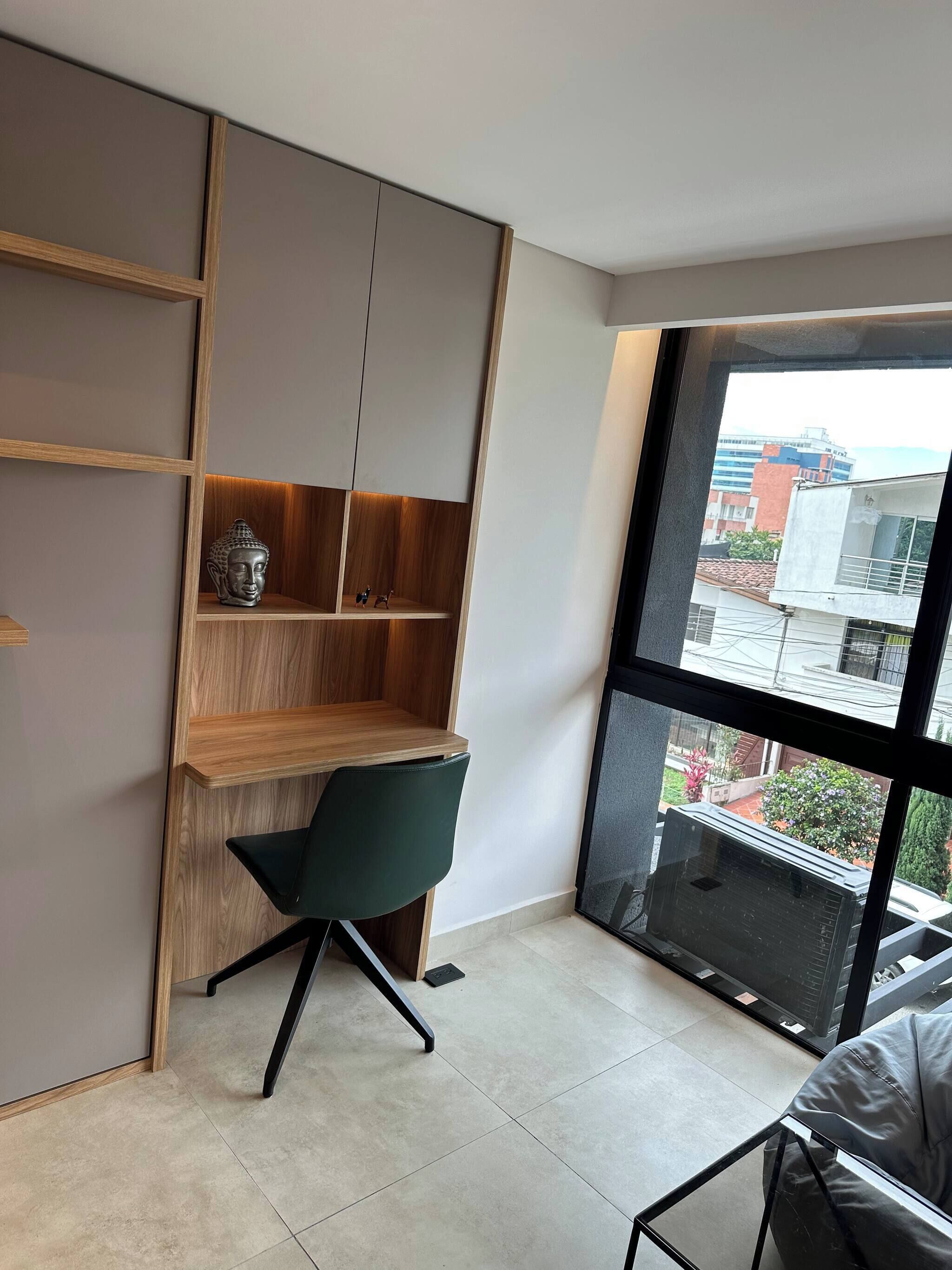 Una habitación moderna con un ventanal grande, un escritorio de madera, una silla verde y una estatua de Buda.