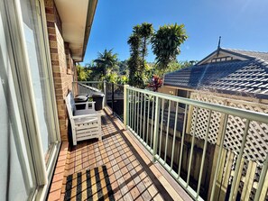 A balcony with a white bench, a trash bin, and a metal railing. - Boambee Beauty - Family Pad - 3 bed - Pets Welcome (Boambee East)