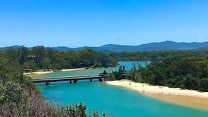 Un paisaje costero con un puente, una playa y colinas boscosas.
