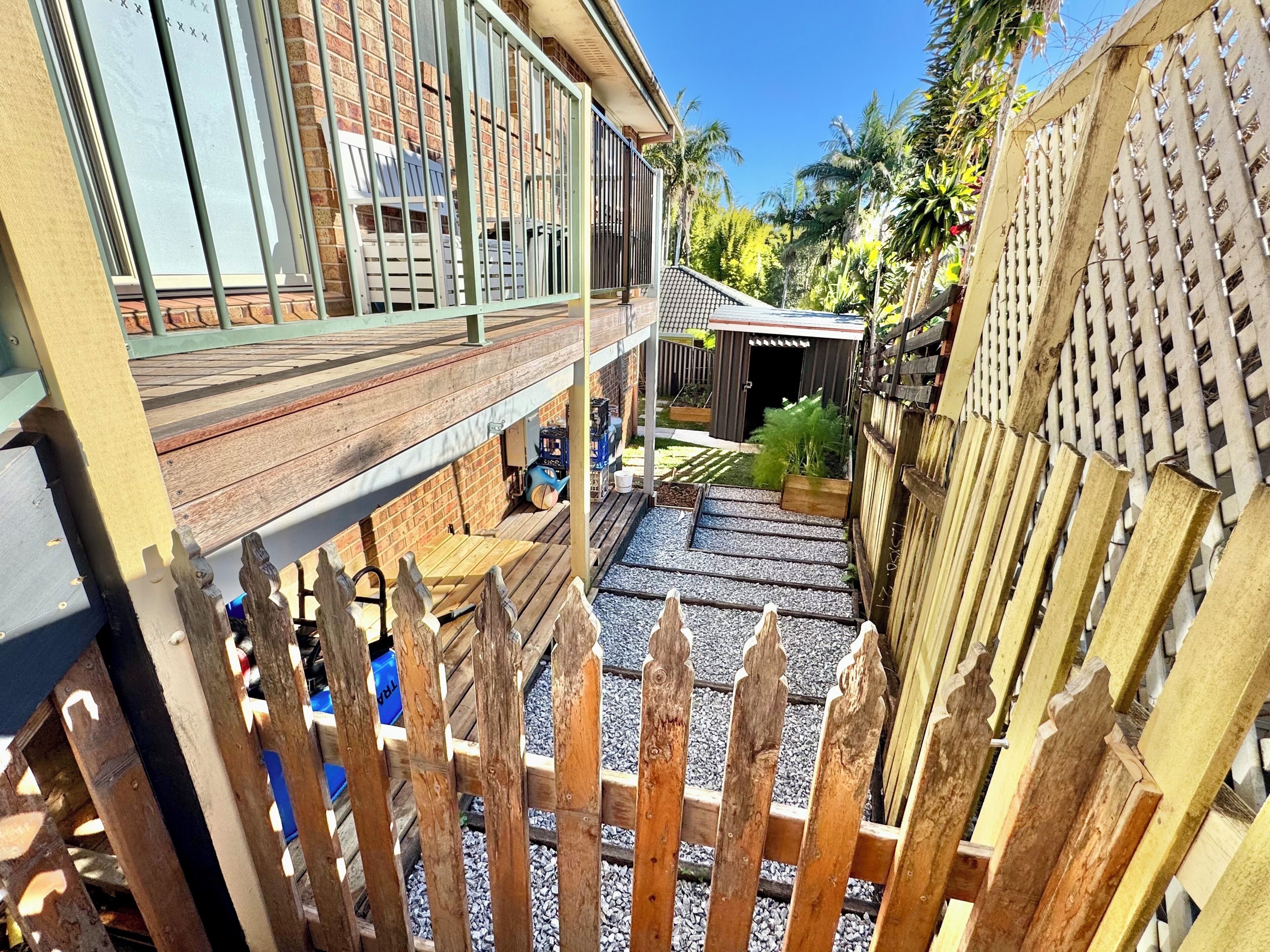 Un patio con cerramiento de madera, zona de estar cubierta y un pequeño jardín.